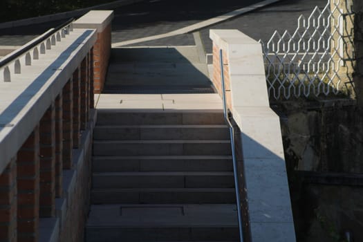 A set of stone steps transitions to a pathway, illuminated by soft morning sunlight, with a brick railing adding a rustic touch to the urban environment.
