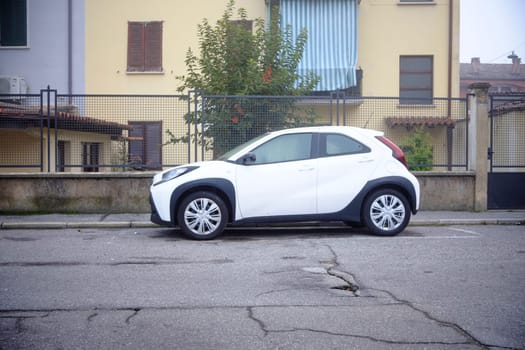 Cremona, Lombardy, Italy - November 7th 2024 Modern compact toyota aygo car parked on a cracked asphalt road near a residential building, showcasing urban parking challenges