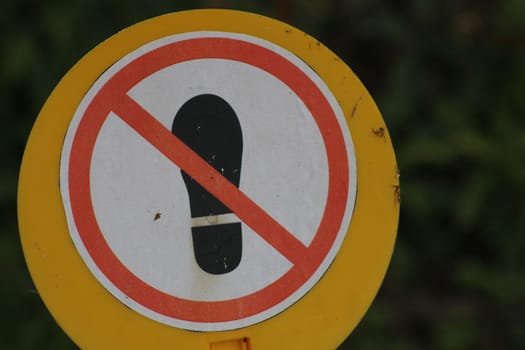 A yellow circular sign displays a red prohibition symbol over a footprint, warning against entering restricted areas in nature. This visual clearly indicates limitations.