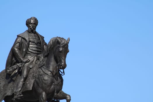 A detailed bronze statue depicts a historical figure on horseback, proudly standing against a vibrant blue sky, capturing attention in a public space.