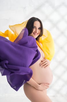 Happy pregnant woman wrapped in color cloth cropped shot in a sunny room