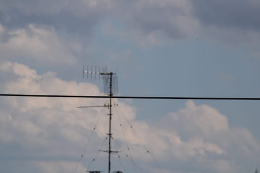 The radio antenna rises prominently against a bright sky filled with scattered clouds, creating a striking contrast during the afternoon hours.