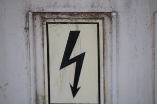 A warning sign featuring a stylized lightning bolt symbol clearly indicates the presence of electrical hazards near a building's entrance. Safety measures are highlighted.