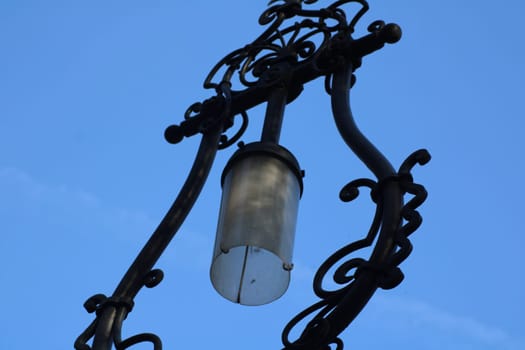 A beautifully crafted street lamp features decorative metalwork and a glass lantern, creating a charming atmosphere on a sunny day, highlighting urban artistry.