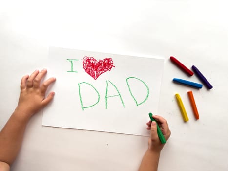 Childs drawing with I love dad message and colorful crayons on white paper.