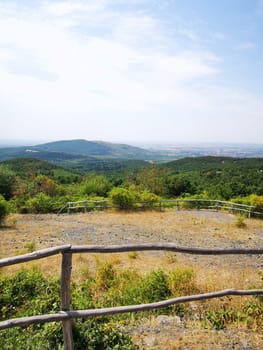 A breathtaking panorama reveals a sprawling green valley, bordered by hills and a wooden fence, illuminated by the bright afternoon sun.