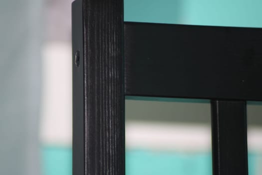 The black wooden chair leg captures attention with its sleek finish and craftsmanship while contrasting against a bright turquoise background setting.