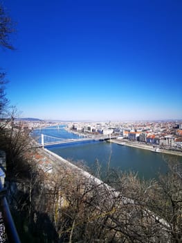 This breathtaking view captures the Danube River flowing through Budapest, revealing iconic bridges and vibrant buildings against a cloudless blue sky.