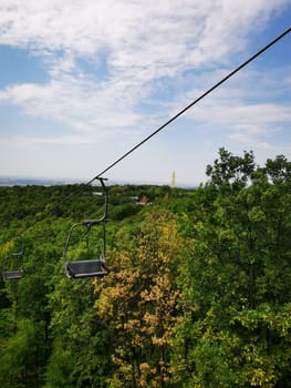 A chairlift glides above a vibrant forest, offering breathtaking views of the landscape below under a clear blue sky on a beautiful day.