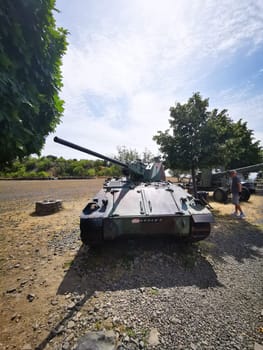 A vintage tank is prominently displayed on a gravel path, surrounded by lush greenery and other military vehicles, capturing the essence of a peaceful afternoon.