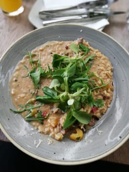 A hearty bowl of creamy risotto is topped with fresh greens, highlighting a rustic design at a charming eatery during a relaxed midday meal.