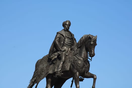 A prominent equestrian statue features a historical figure majestically seated on a horse. The clear blue sky provides a striking backdrop to the artwork.
