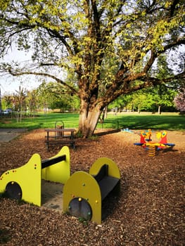 Children enjoy an outdoor playground featuring vibrant play equipment surrounded by a lush green landscape and beautiful trees on a sunny day.