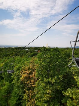 Riding a chairlift provides a breathtaking perspective of verdant trees below and rolling hills in the background under a bright blue sky, revealing nature's beauty.