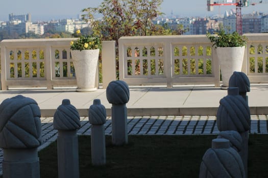 The outdoor area showcases a collection of abstract sculptures made of stone, arranged neatly on a paved surface with a vibrant city skyline in the background.