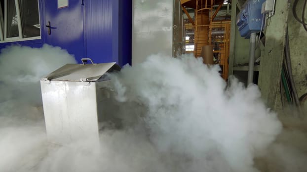 Dense steam billowing up and out from a stainless steel container situated in an industrial setting environment. Stock Clip