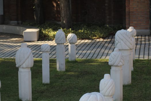 The garden features several white marble sculptures designed to look like yarn balls and spools, artfully arranged on green grass with nearby brick pathways and plants.