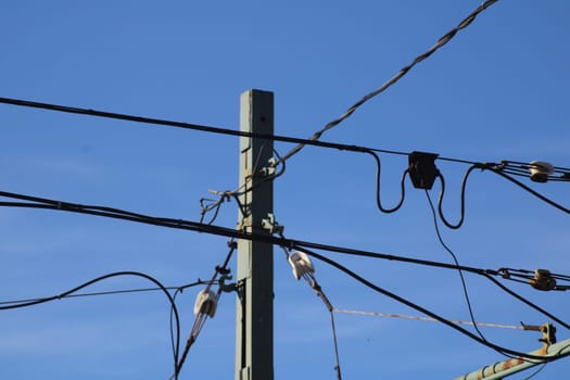 Utility poles and power lines stretch across a bright blue sky, illustrating essential electrical infrastructure. The composition highlights the complexity of modern energy distribution.