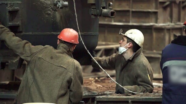 Technical workers collaborating on machinery in an industrial setting, showcasing teamwork and safety. Stock Clip