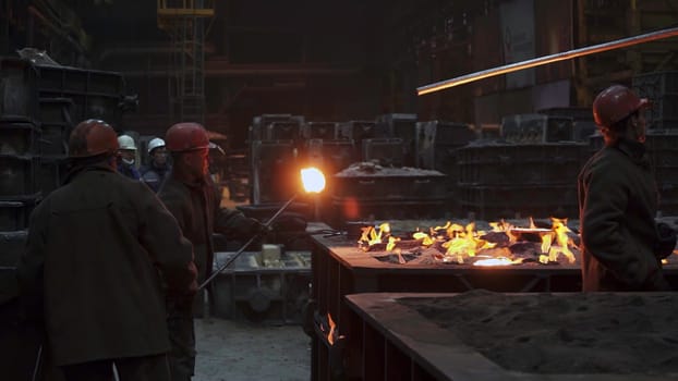 Skilled workers pour molten metal in a dimly lit foundry, showcasing exceptional industrial craftsmanship. Stock Clip