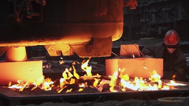 In a dynamic industrial setting, a skilled worker deftly shapes molten metal amidst intense flames and smoke. Stock Clip