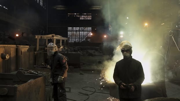 Workers are intensely engaged in the intricate process of metal casting within a dimly lit industrial foundry. Stock Clip