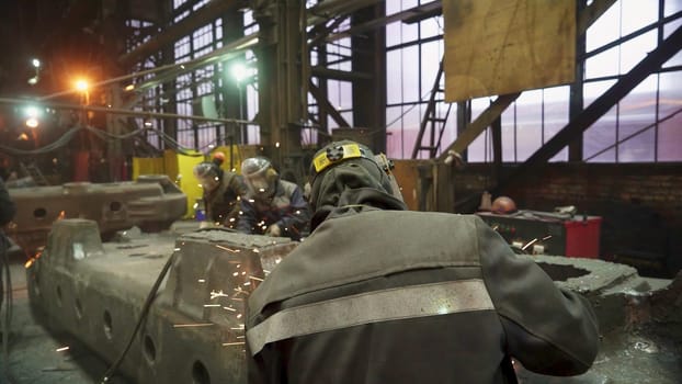 A skilled team is expertly welding metal components in a vast industrial facility at dawn, showcasing precision. Stock Clip