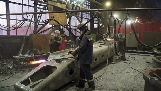 Factory workers in an industrial environment diligently creating metal components using specialized welding equipment. Stock Clip