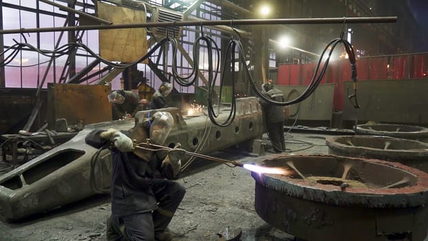 Workers engaged in the meticulous process of metal fabrication within an industrial facility utilizing heavy machinery. Stock Clip