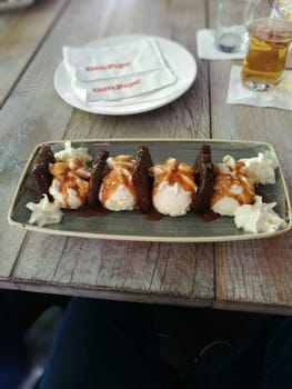 Five chocolate taco shells filled with creamy vanilla ice cream drizzled with caramel sauce are served on a rustic wooden table. A refreshing drink awaits nearby.