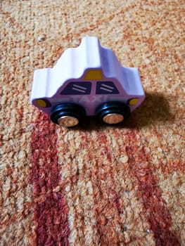 A brightly colored wooden toy car rests on a vibrant carpet, inviting children to engage in imaginative play during a sunny afternoon.