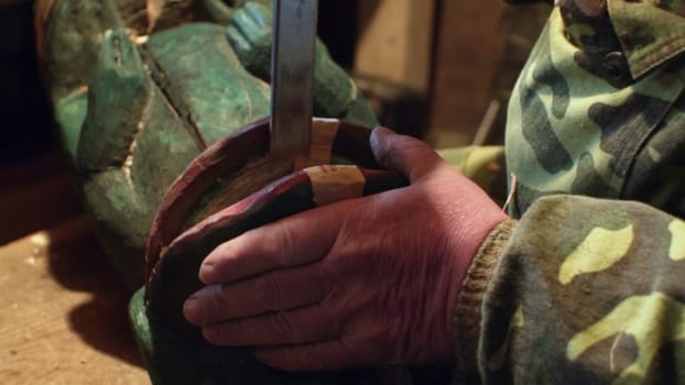 Close up of skilled hands meticulously repairing old military boots with detailed green camouflage patterns. Stock Clip