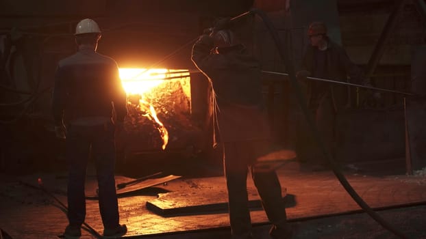 In a dimly lit foundry setting, two skilled workers expertly control and manage the molten metal process. Stock Clip