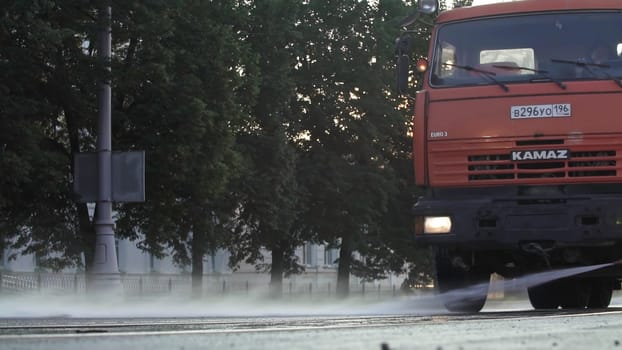 Tbilisi, Georgia - September 29, 2023: A bright red truck drives swiftly along a wet street, splashing up water as the sun rises behind the trees. Stock Clip