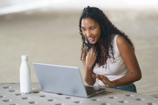 A young woman expresses immense joy and excitement while enthusiastically interacting with her laptop in a modern contemporary setting, embodying a perfect blend of technology and creativity
