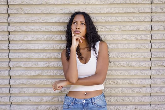 A thoughtful and introspective young woman with beautiful curly hair poses gracefully against a textured wall, showcasing a captivating moment of deep contemplation and reflection about life