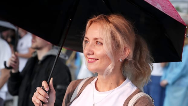 Georgia, Tbilisi - July 20, 2024: A joyful and cheerful woman finds delight in a rainy day, holding a vibrant umbrella amidst a bustling crowd. Clip