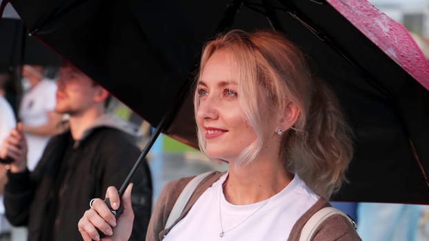 Georgia, Tbilisi - July 20, 2024: A joyful and cheerful woman finds delight in a rainy day, holding a vibrant umbrella amidst a bustling crowd. Clip