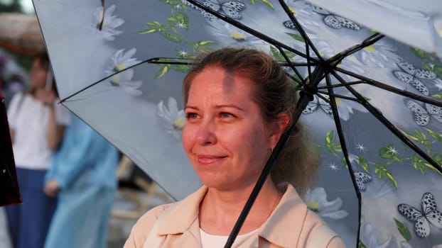 Georgia, Tbilisi - July 20, 2024: A serene moment of a woman sitting under a floral umbrella, embracing nature while enjoying the gentle rain. Clip