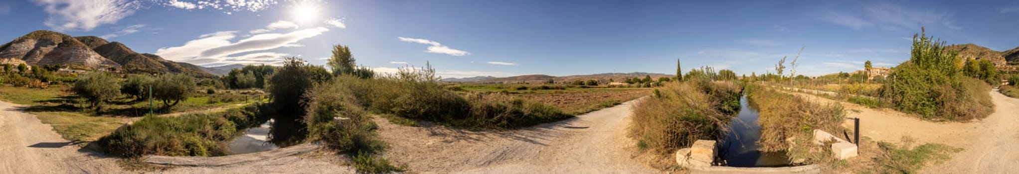 This truly stunning landscape showcases lush greenery, a tranquil water channel, and majestic mountains set against a clear blue sky, making it perfect for themes related to nature and agriculture