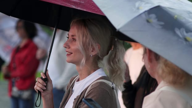 Georgia, Tbilisi - July 20, 2024: Two joyful women share colorful umbrellas and laugh heartily while enjoying a rainy day in a lively city. Clip