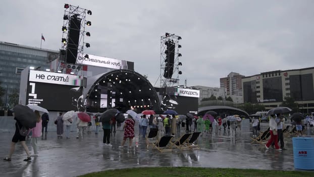 Georgia, Tbilisi - July 20, 2024: An exciting outdoor event unfolds under rainy skies, featuring a large stage and enthusiastic attendees. Clip