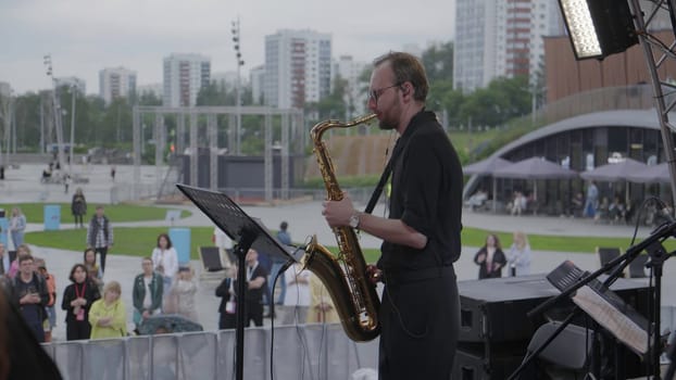 Georgia, Tbilisi - July 20, 2024: In a vibrant outdoor concert setting, a talented saxophonist mesmerizes an engaged audience amid city buildings. Clip