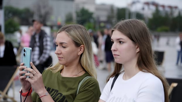 Georgia, Tbilisi - July 20, 2024: Two women are engaged in taking photos at a lively outdoor gathering, showcasing modern connections. Clip