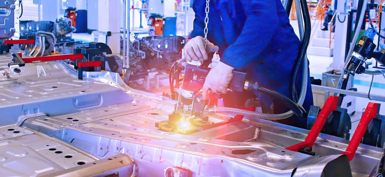 A technician operates specialized robotic equipment to securely assemble a vehicle chassis in a high-tech automotive production environment. Bright lights enhance the intricate details of the assembly process.