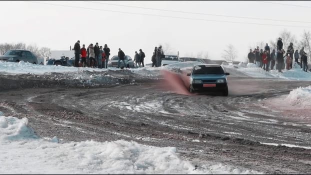 Experience winter driving as a skilled driver navigates through snow, drifting gracefully on a dirt road, impressing a captivated crowd nearby