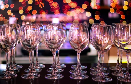 A collection of sparkling wine glasses is carefully arranged at a table, illuminated by dazzling, colorful lights during a celebration.