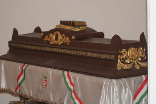 A beautifully carved wooden object rests on a table adorned with a decorative cloth featuring the Hungarian flag. The craftsmanship is evident in its intricate details and design.