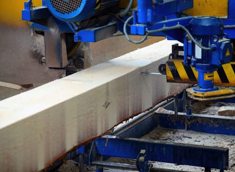 A large beam of wood is being precisely cut by a machine in a lumber mill, showcasing the woodworking process.