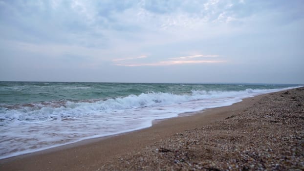 Experience the serene beauty of a sandy beach with crashing waves on a cloudy day. The rhythmic ocean sounds create a calming atmosphere